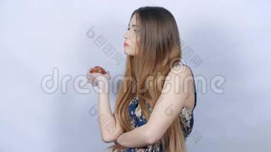 年轻的美女，长发，在灰色背景下吃苹果。